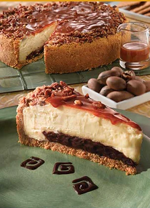 A slice of turtle cheesecake with caramel and pecans beside a whole cheesecake